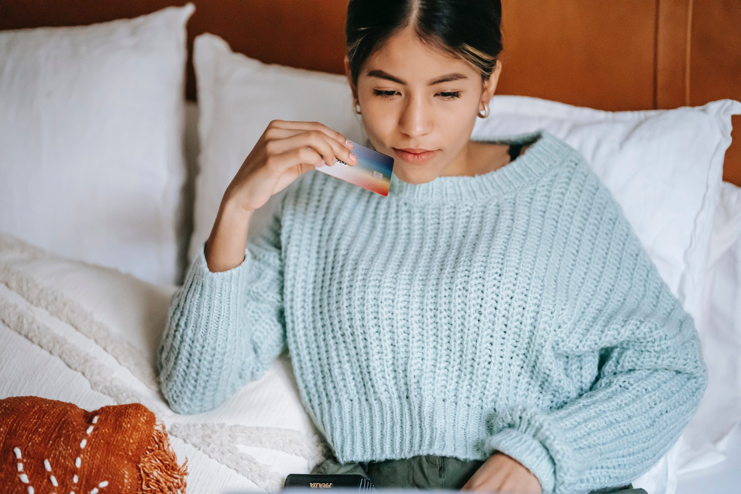 woman sitting on a bed holding a credit card while typing on a laptop